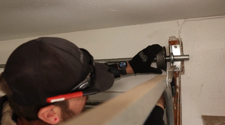 Technician steadying the torsion tube against the end bearing plate at the top corner of a garage door