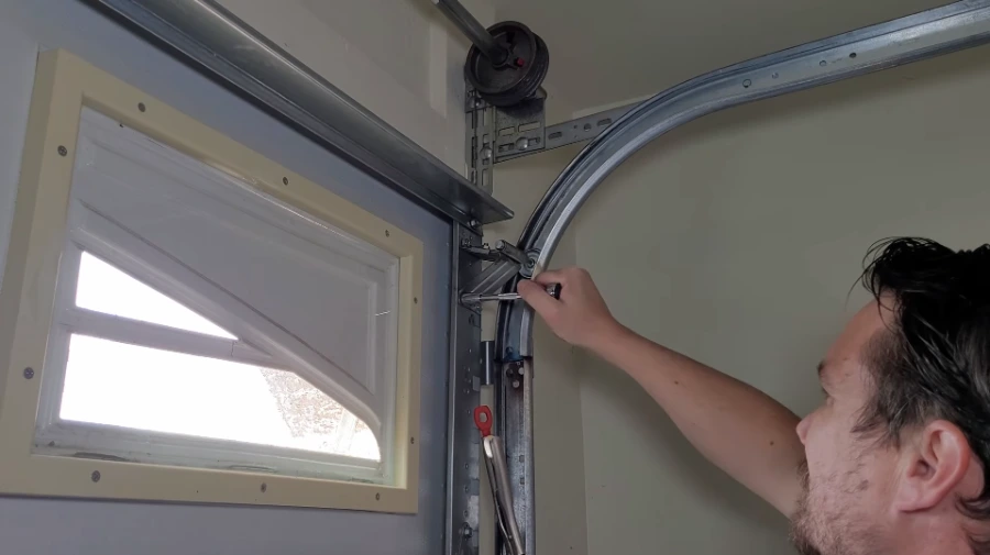 Technician adjusting a garage door hinge and roller bracket on the curved track below the cable drum