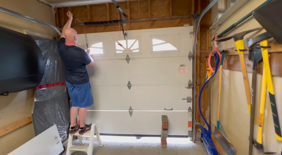 Installer fitting the top section of a new white sectional garage door during a Lubbock installation
