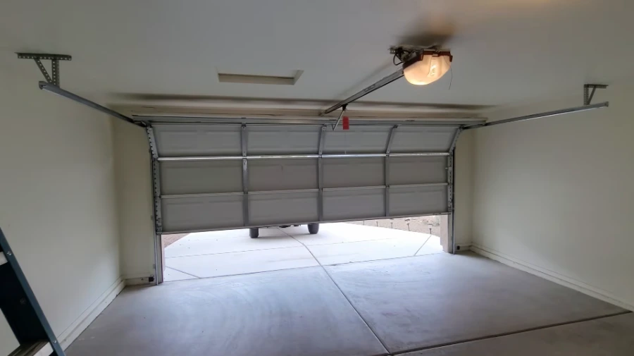 Interior of a two-car garage with the sectional door partly open and the opener light on