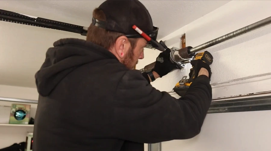 Garage door technician driving a fastener into the centre bearing plate and spring anchor bracket above the door