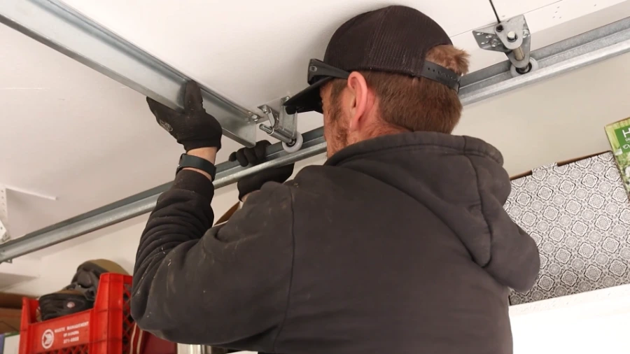 Technician fitting a horizontal garage door track hanger to the ceiling framing to bring the track back into alignment