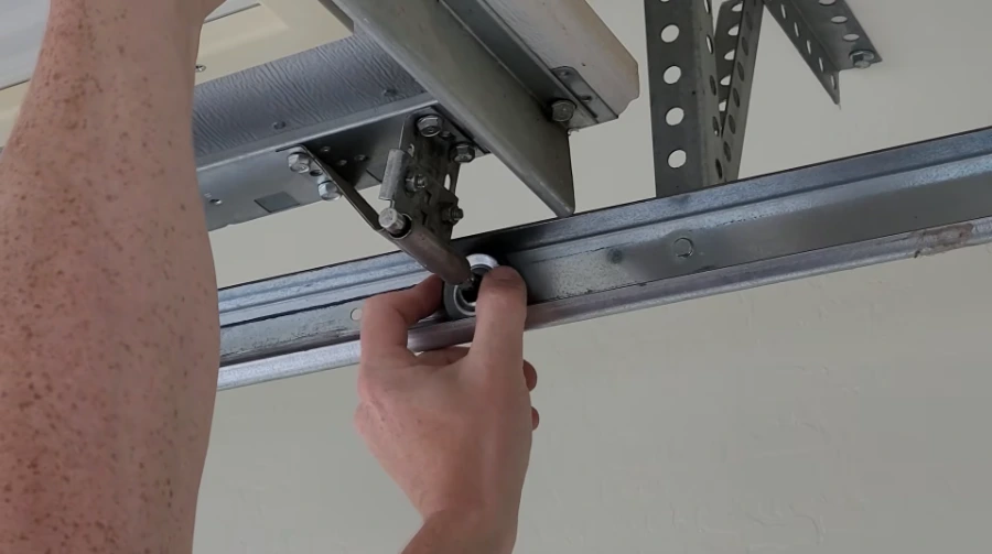 Technician seating a roller into the horizontal garage door track beneath the track hanger brackets